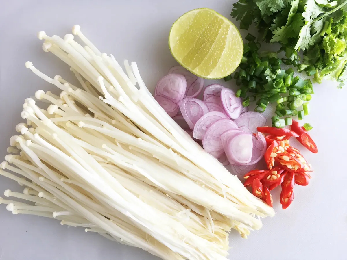 Top view of fresh Thai ingredients including enoki mushrooms, lime, chili peppers, and more for healthy cooking.