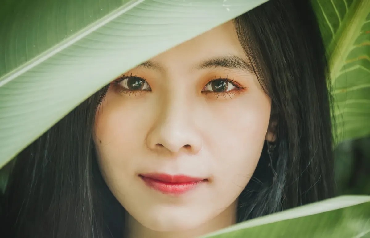 Close-up of young woman's face in nature with leaves framing her beauty.
