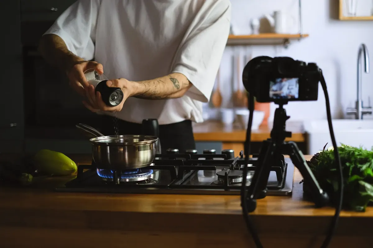 A person seasoning food on a stove while recording a cooking vlog in a modern kitchen.
