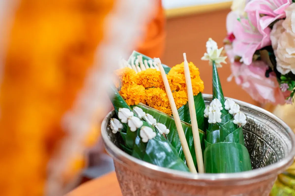 A vibrant Thai floral arrangement featuring marigolds in a silver bowl at a traditional ceremony.