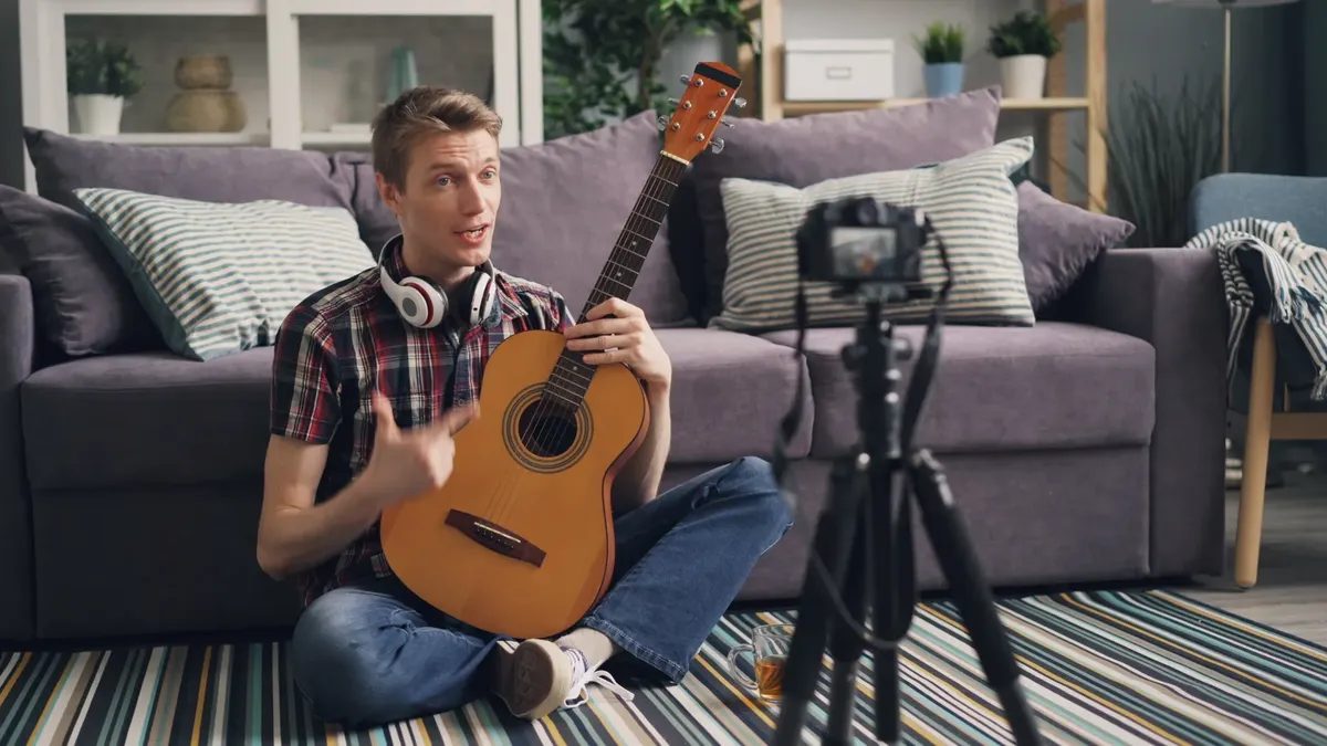 Adult man playing guitar while streaming music video indoors.