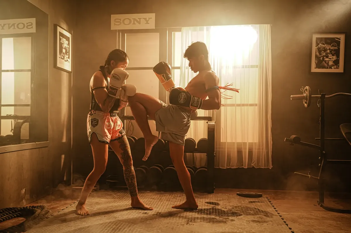 A male and female athlete engage in a dynamic Muay Thai sparring session.