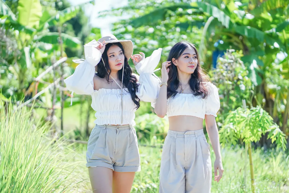 Two Asian women in white crop tops enjoying a sunny day in nature.