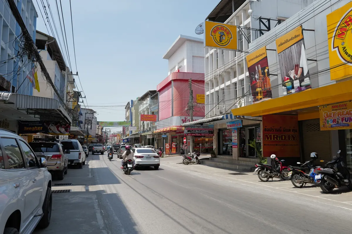元気なタイ市街の風景。車、自転車、色とりどりの店の外観が見える。太陽の下のシーン。